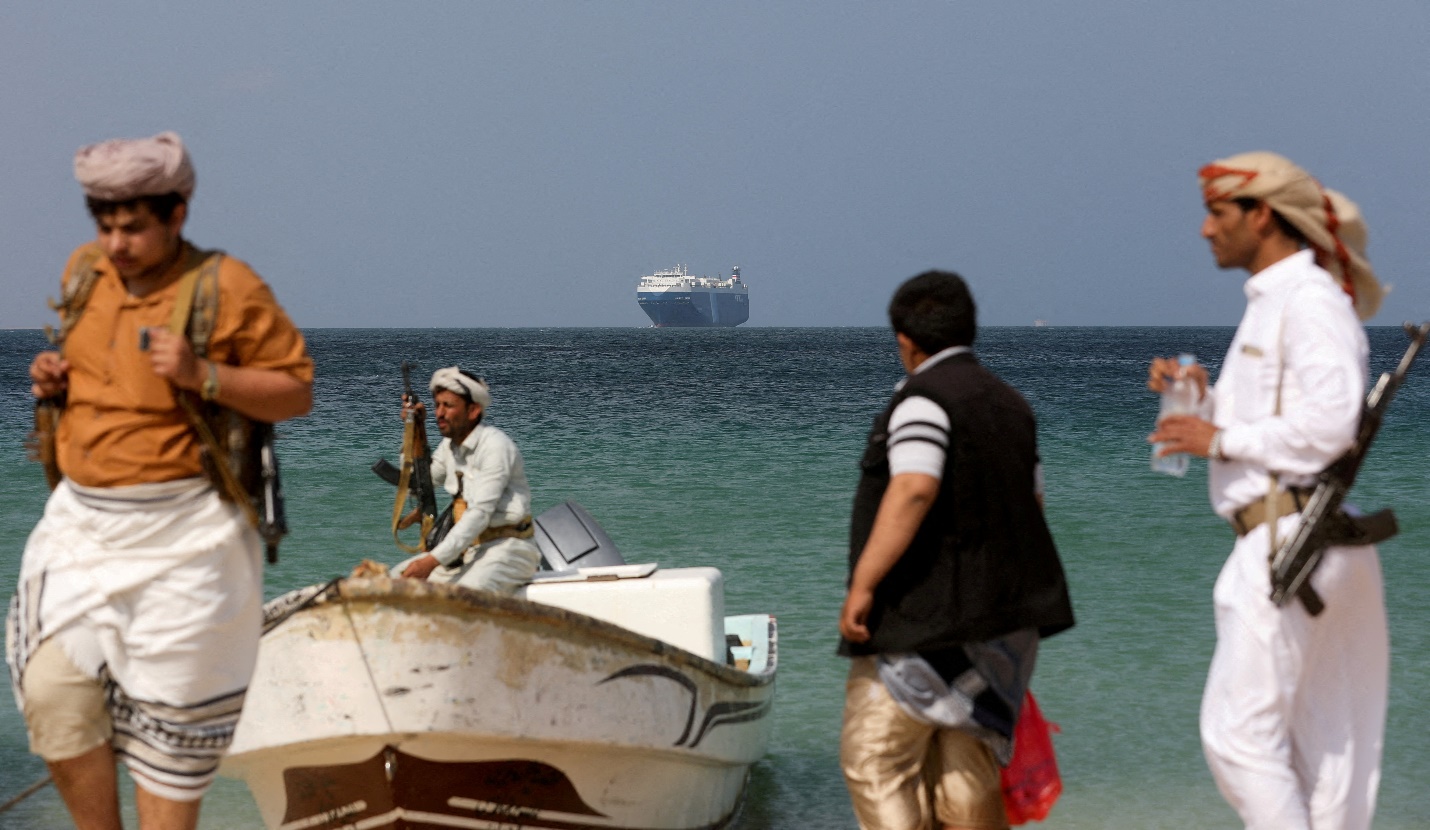 Rebels stand on the beach as the Galaxy Leader commercial ship, seized by Yemen's Houthis last month, is anchored off the coast of al-Salif, Yemen, December 5, 2023 [REUTERS/Khaled Abdullah]